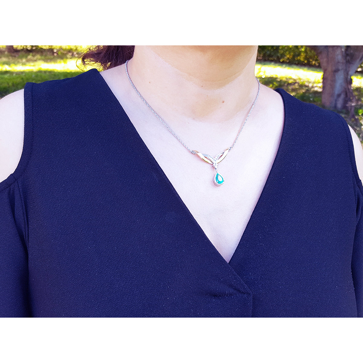 Woman wearing a blue top with a necklace featuring a dangling natural teardrop emerald pendant outdoors.