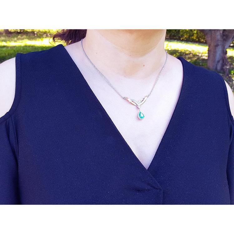 Woman wearing a blue top with a necklace featuring a dangling natural teardrop emerald pendant outdoors.
