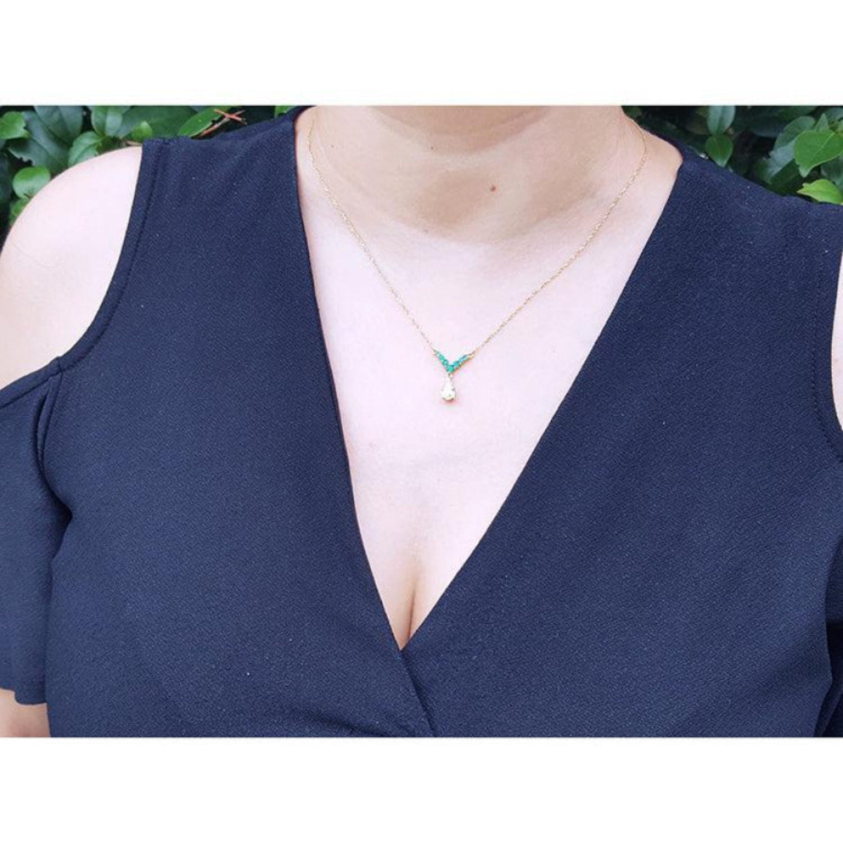 14K gold necklace with a 0.69 ct pear diamond and 0.35 ct round emeralds on a woman's neck.