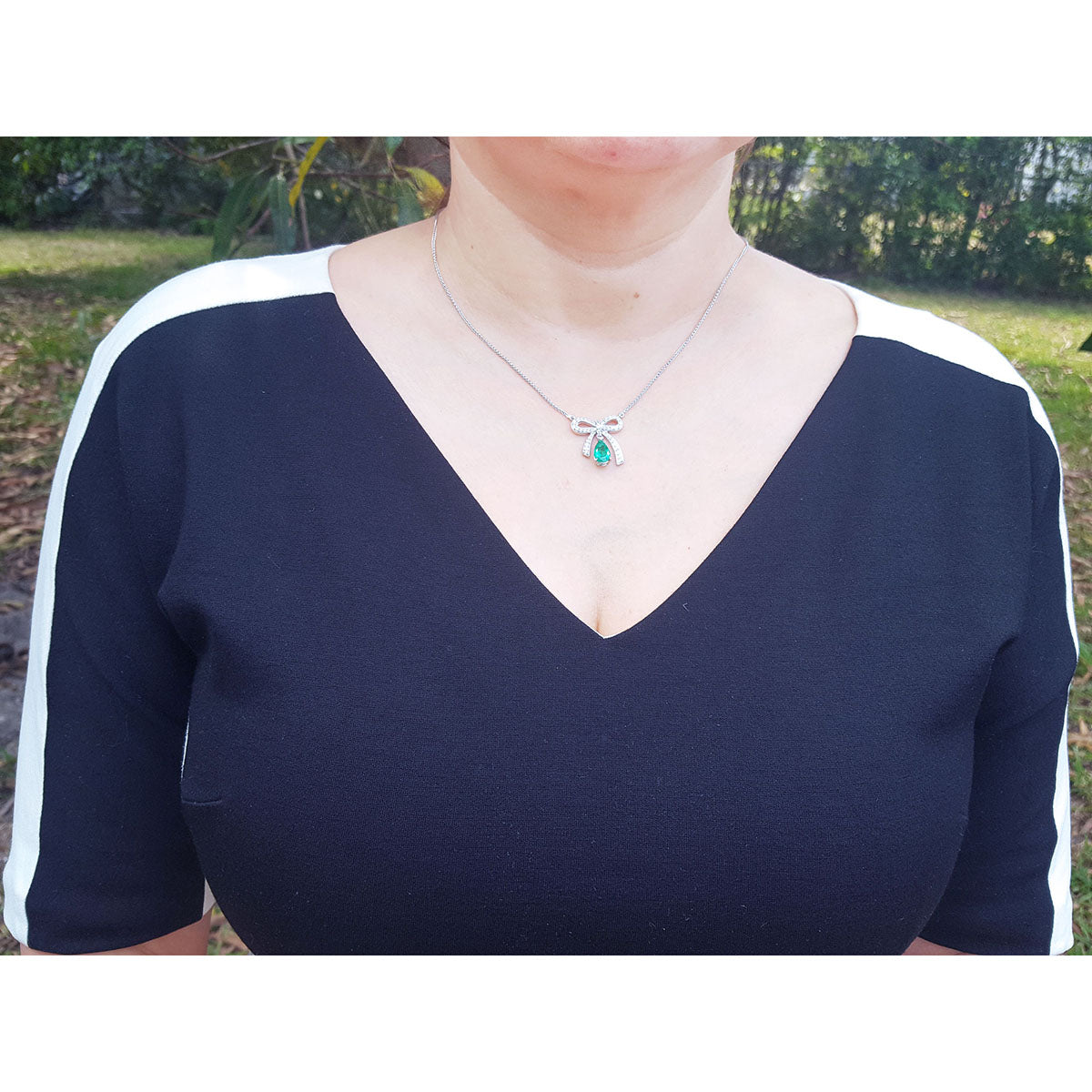 Woman wearing Bow tie Colombian emerald necklace pear cut with high quality natural diamonds, standing outdoors.