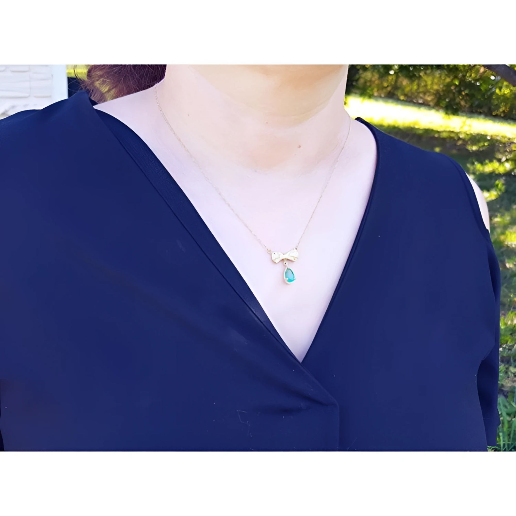 18K yellow gold bow-tie emerald necklace with a dangling pear-shaped emerald and yellow diamond accents.