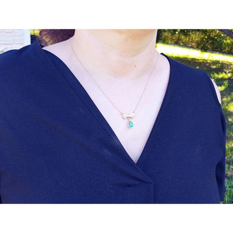 18K yellow gold bow-tie emerald necklace with a dangling pear-shaped emerald and yellow diamond accents.