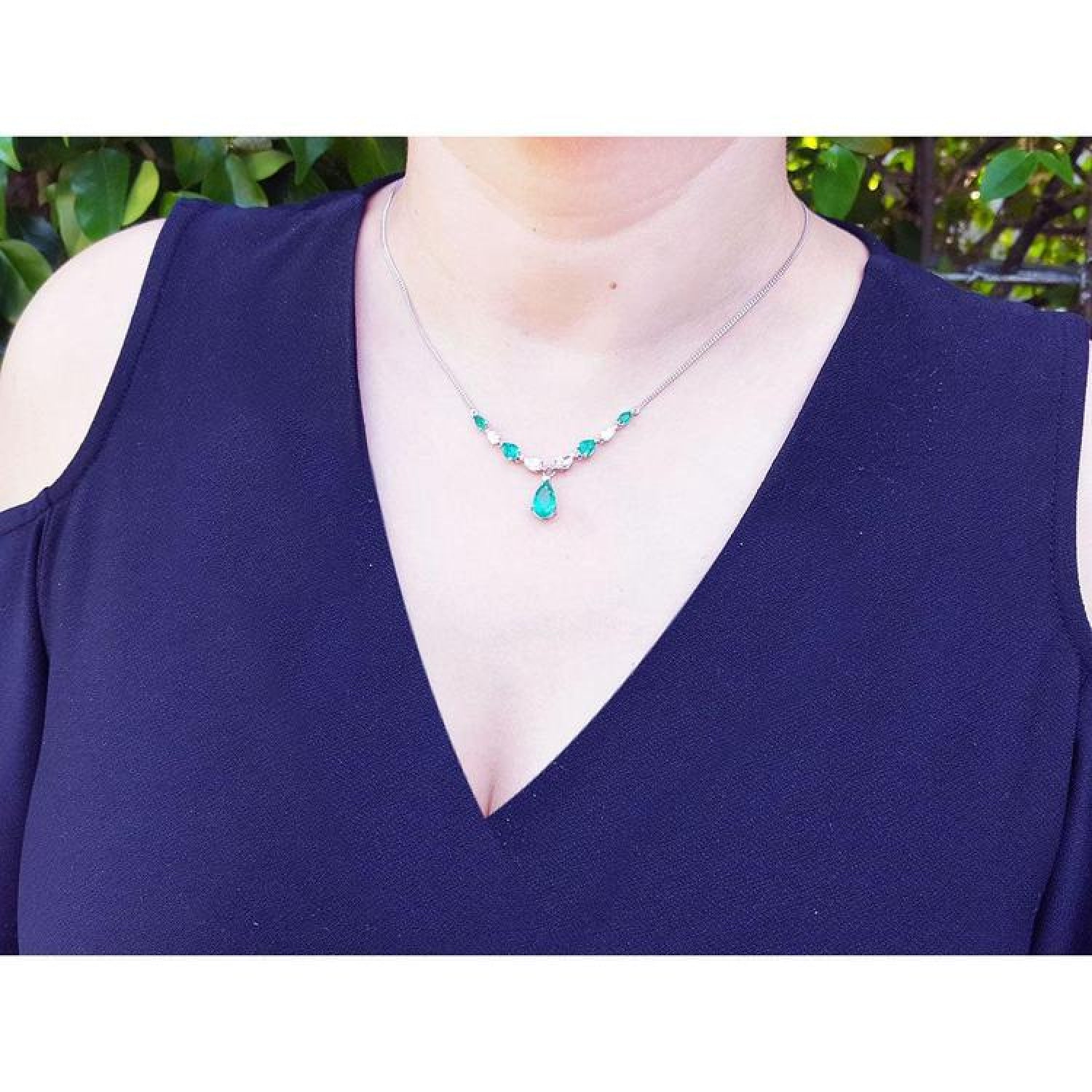 14k white gold necklace with pear-shaped emeralds and diamonds on a model.