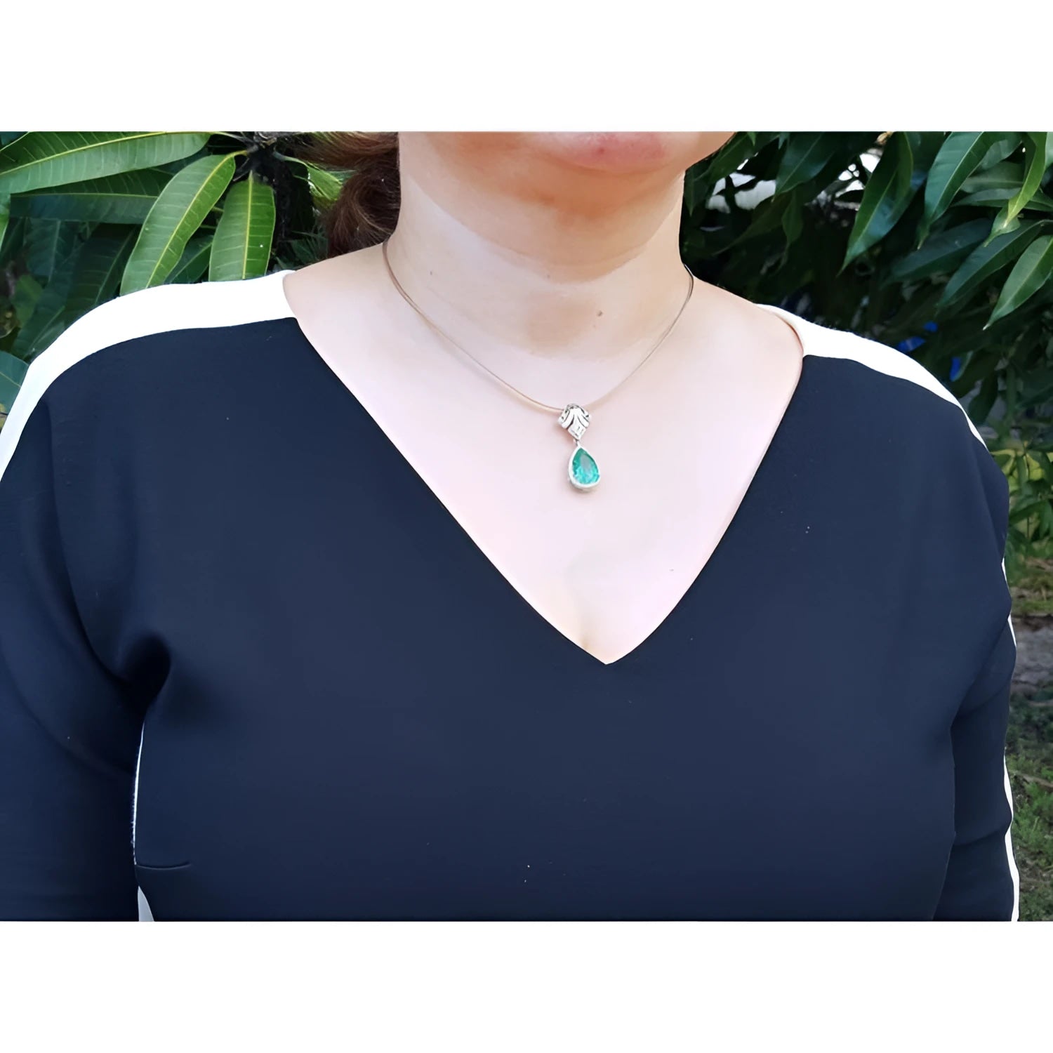 Woman wearing an 18K gold emerald and diamond enhancer necklace with a pear-shaped green emerald.