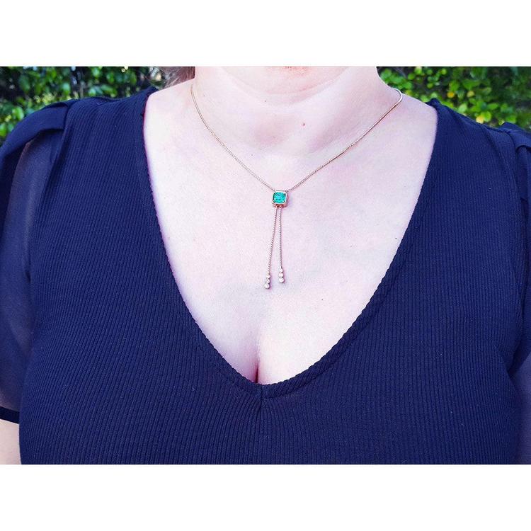 Emerald lariat necklace with an emerald-cut natural emerald, milgrain, prongs, and dangling pearls on a gold box chain.