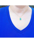 Emerald-cut Colombian emerald pendant with diamond halo on 14k yellow gold chain, worn on a blue shirt.