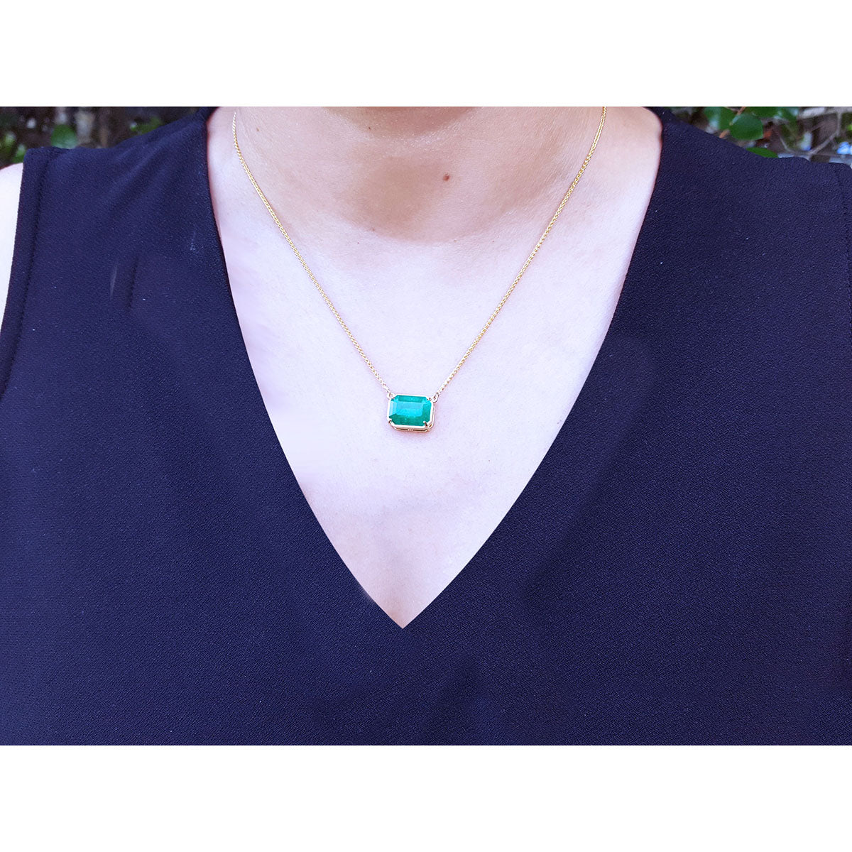 Authentic Colombian Emerald necklace rectangular emerald-cut worn by a woman in a navy blue top.