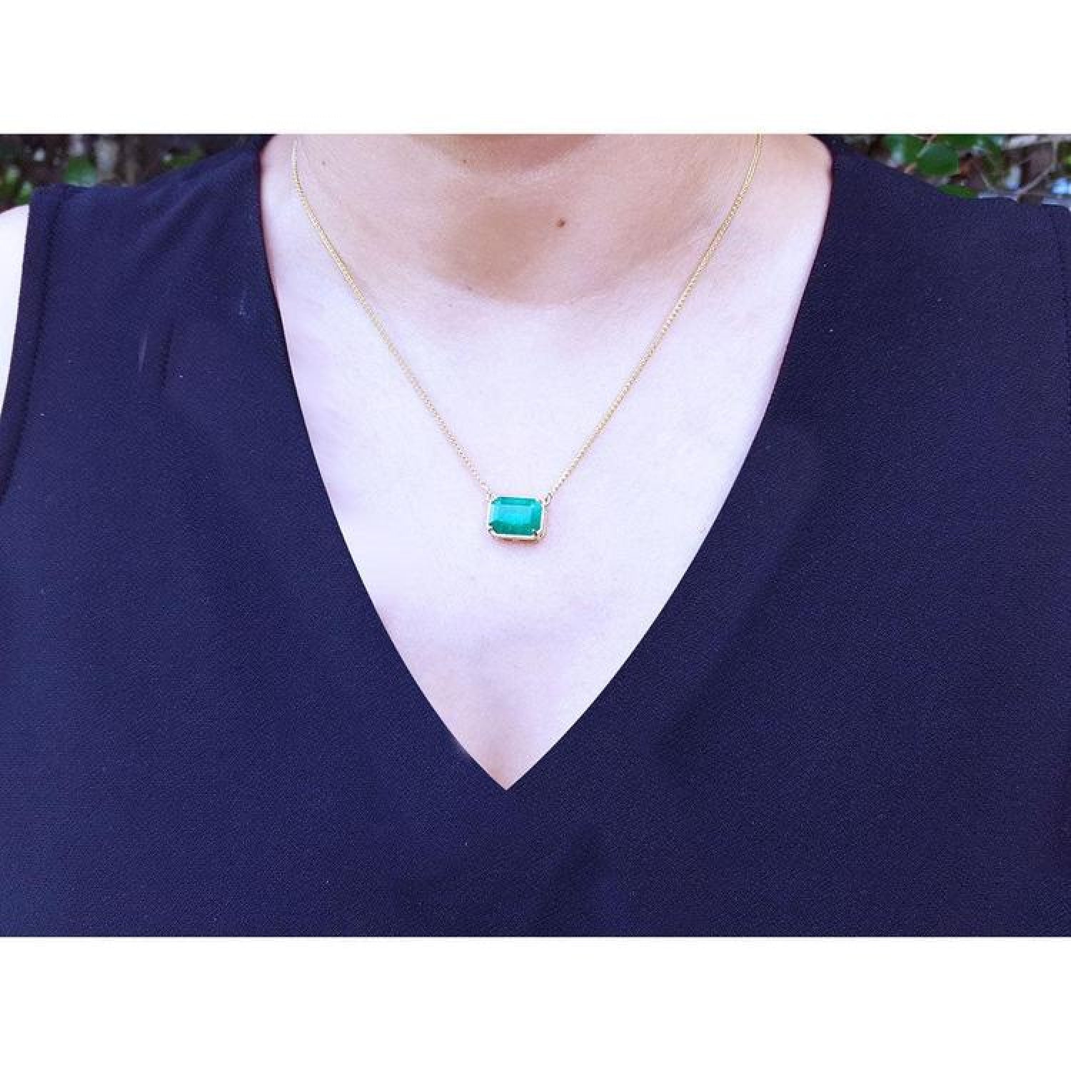 Emerald-cut Colombian emerald solitaire necklace in 18K yellow gold on a woman's chest. styled with a black V-neck top.