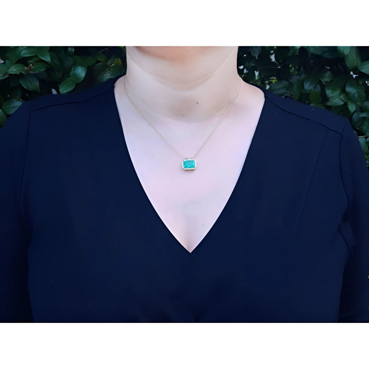 Woman wearing 18K yellow gold necklace with a vibrant deep green emerald solitaire pendant.