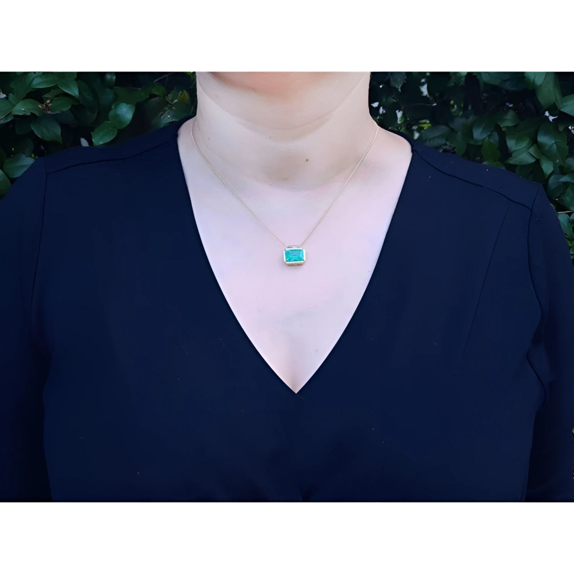 Woman wearing 18K yellow gold necklace with a vibrant deep green emerald solitaire pendant.
