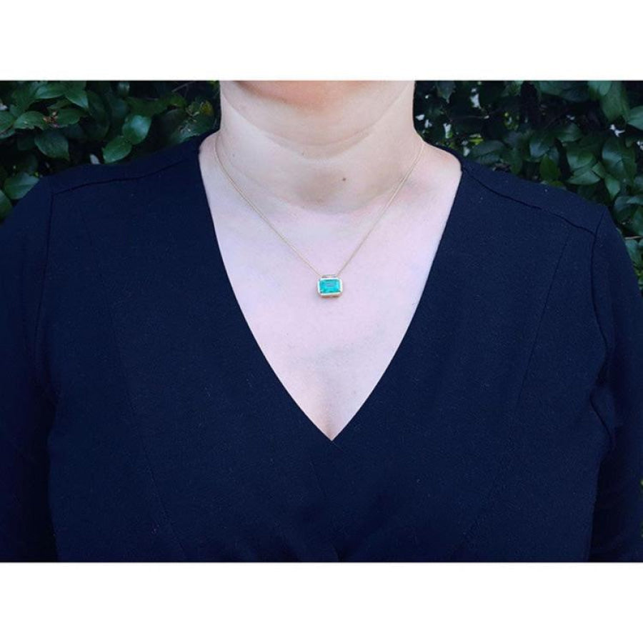 Woman wearing 18K yellow gold necklace with a vibrant deep green emerald solitaire pendant.
