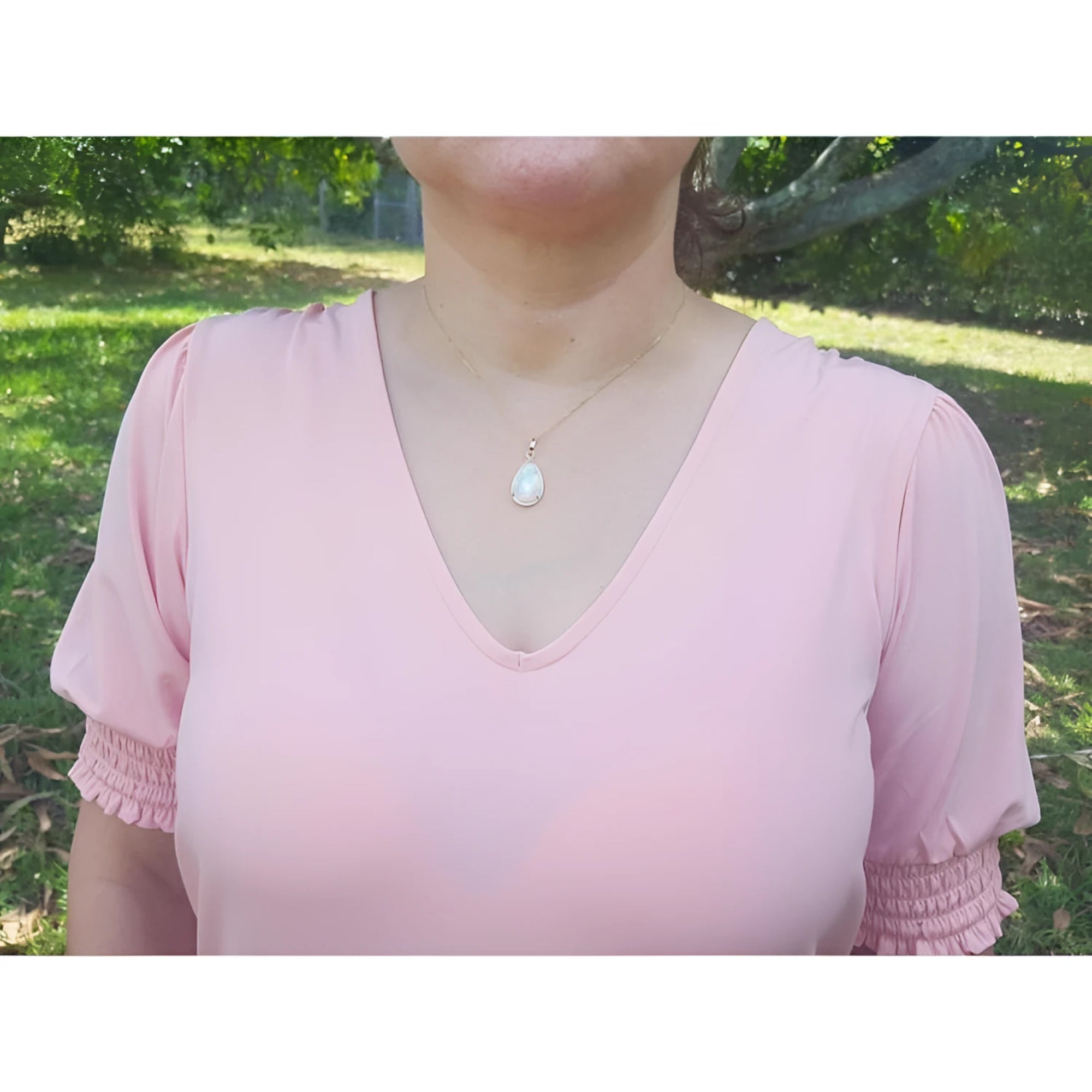 White Ethiopian opal pendant in 14K yellow gold, worn on a woman's neck over a pink shirt.
