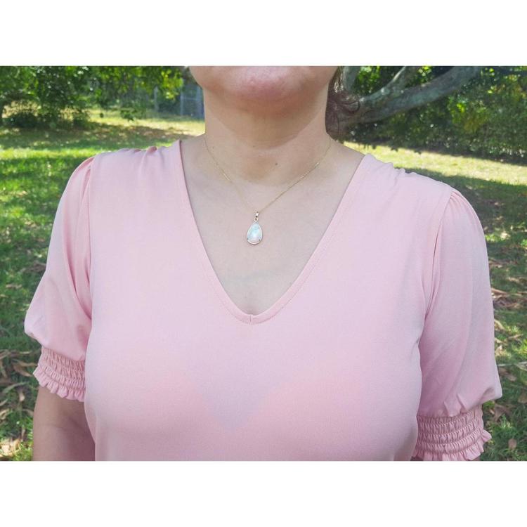 White Ethiopian opal pendant in 14K yellow gold, worn on a woman's neck over a pink shirt.
