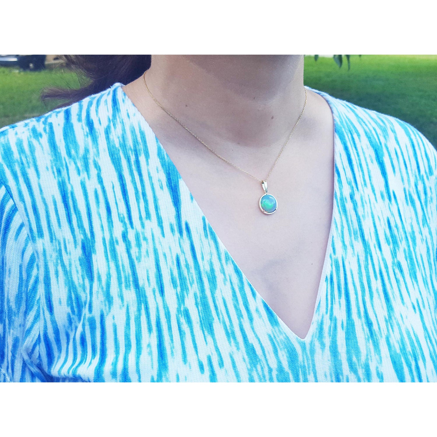 Person wearing a blue and white patterned top with a necklace featuring a Welo opal gold pendant. pendant.