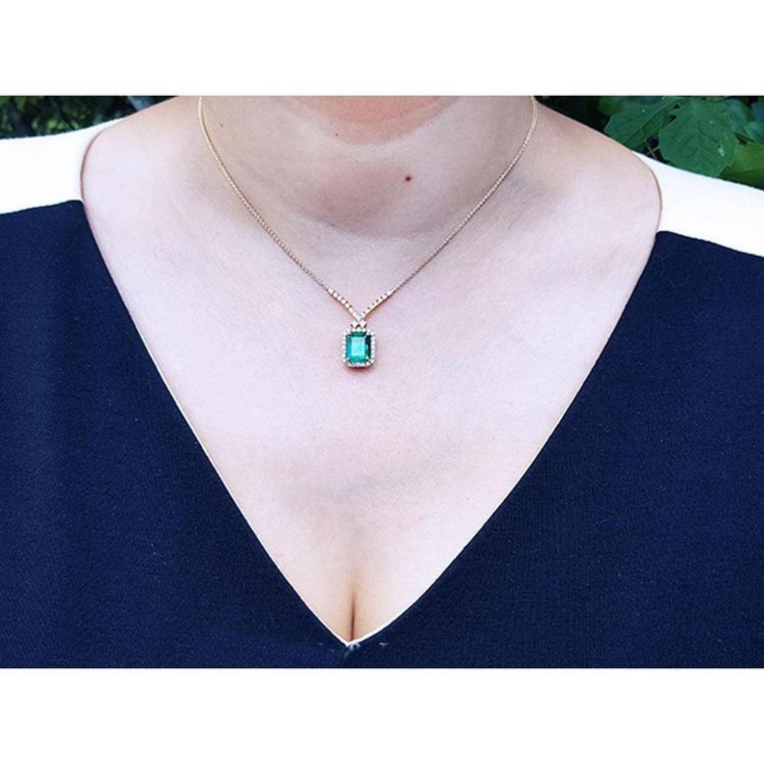 Emerald necklace with halo natural diamonds on a 14K yellow gold chain, worn on a woman's neck.