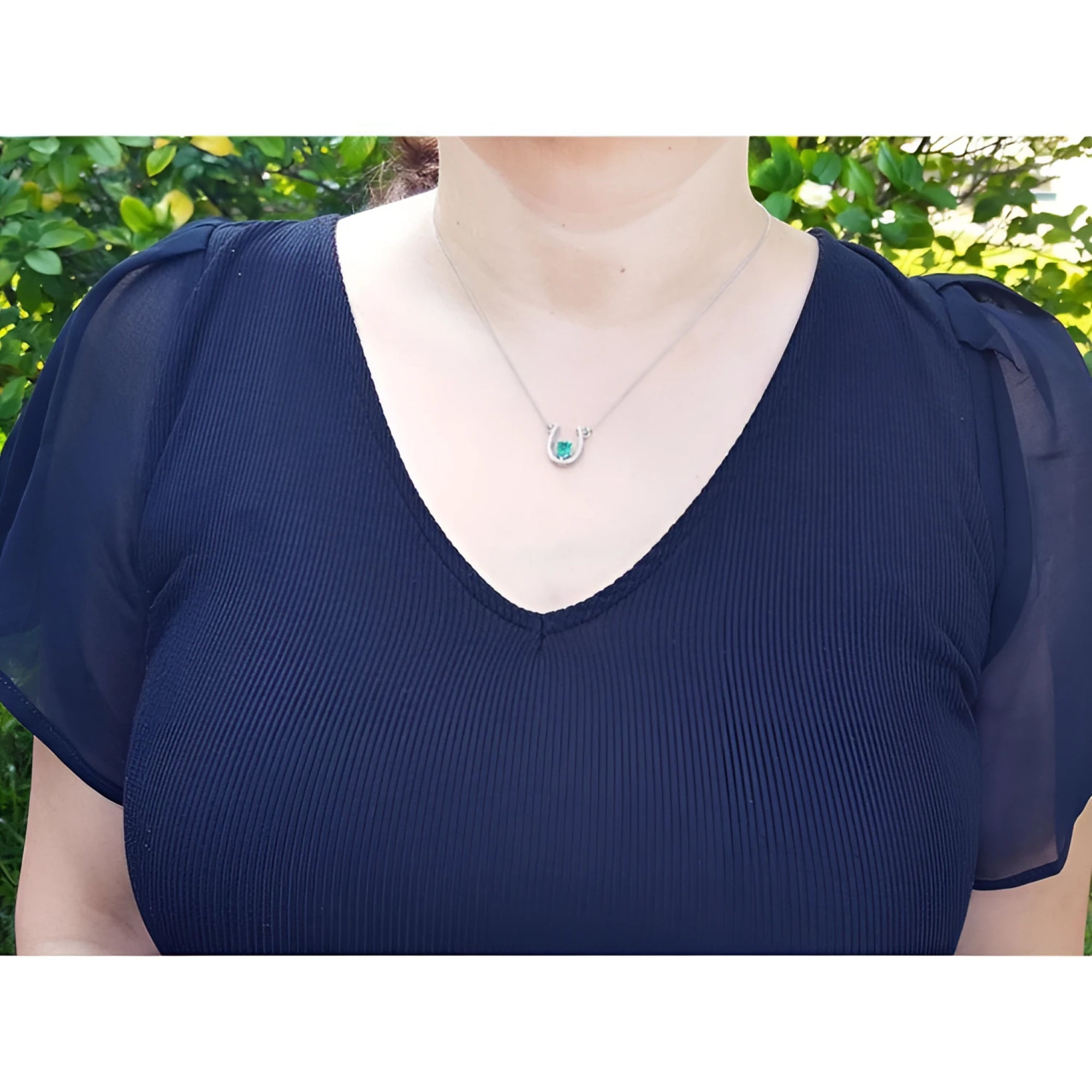 Woman wearing a 14K white gold horseshoe necklace with a green oval emerald and diamonds.