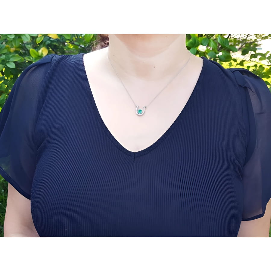 Woman wearing a 14K white gold horseshoe necklace with a green oval emerald and diamonds.