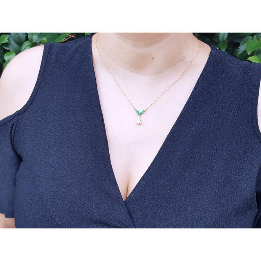 14K gold necklace with a 0.69 ct pear diamond and 0.35 ct round emeralds on a woman's neck.