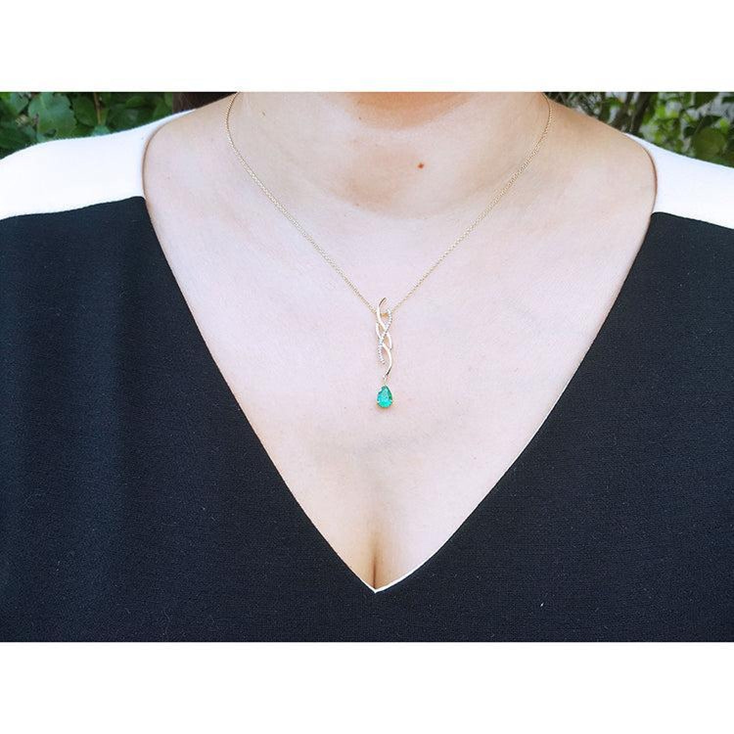 14K yellow gold twisted slider necklace with a pear-shaped Colombian emerald pendant on a woman's neck.