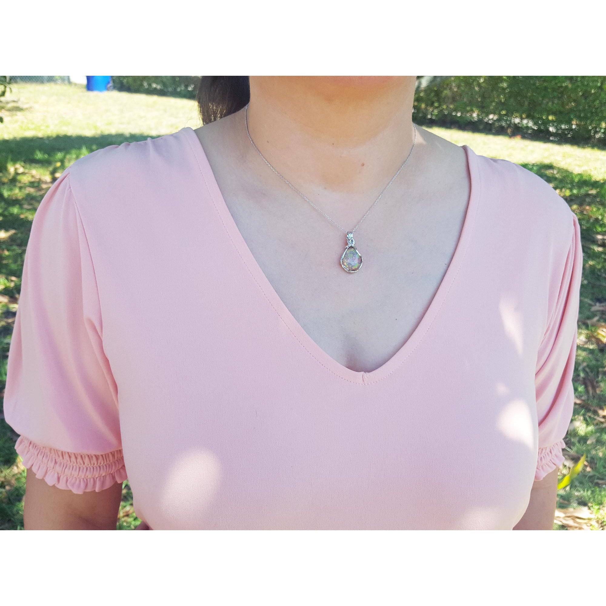 Person wearing a pink blouse with a silver opal necklace against a blurred natural background.