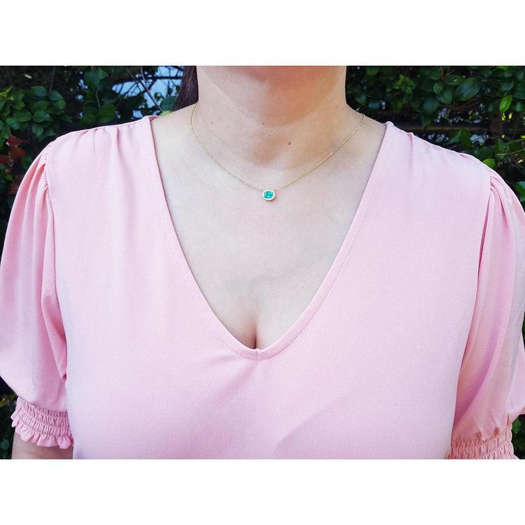 Oval Muzo emerald necklace in 14K yellow gold, worn on a woman in a pink top.
