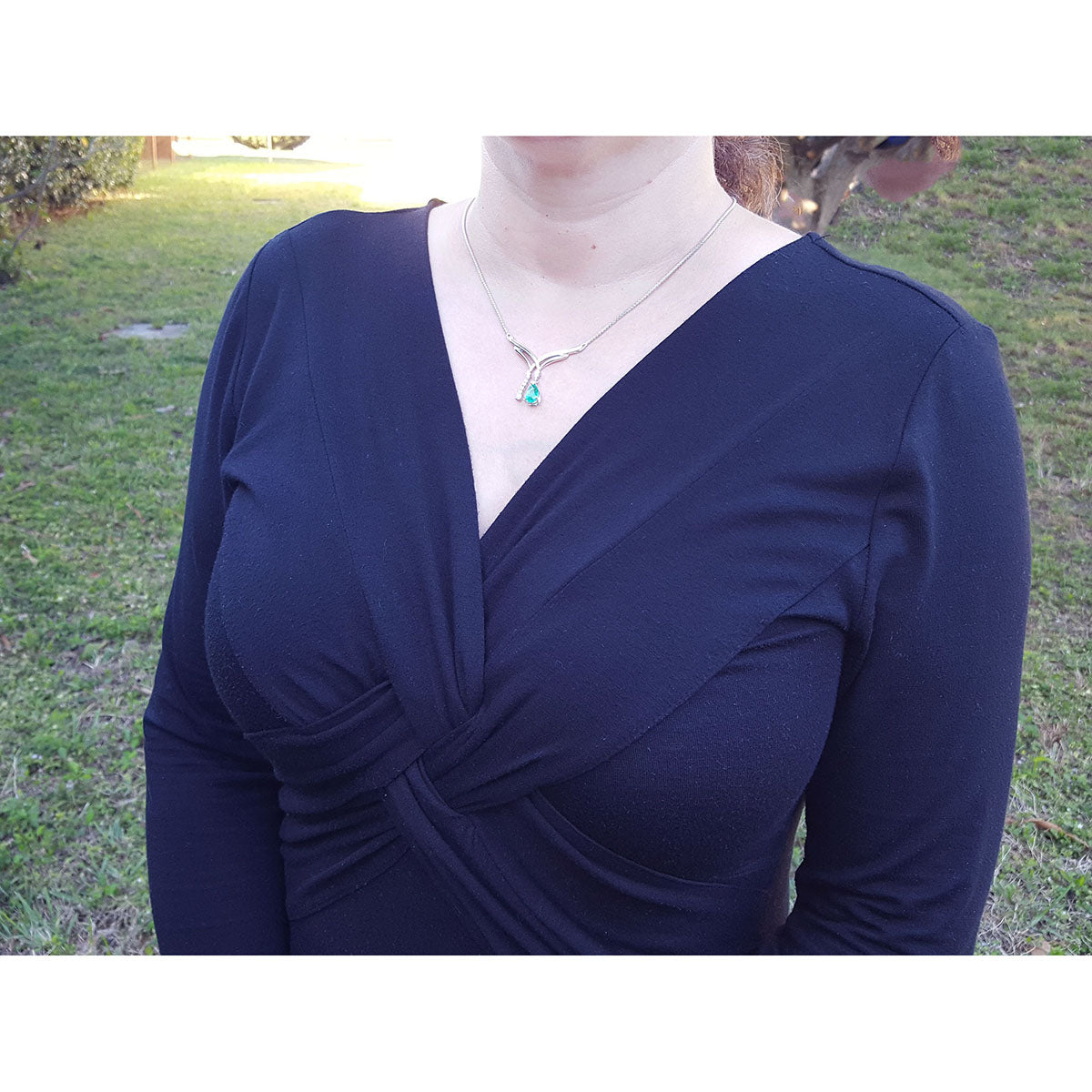Woman dressing a 14k white gold emerald necklace natural pear cut with accent diamonds 