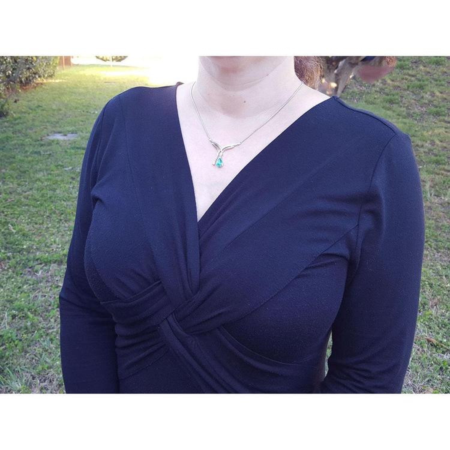 14K white gold necklace with a pear-shaped emerald and diamond chevron pendant on a woman.