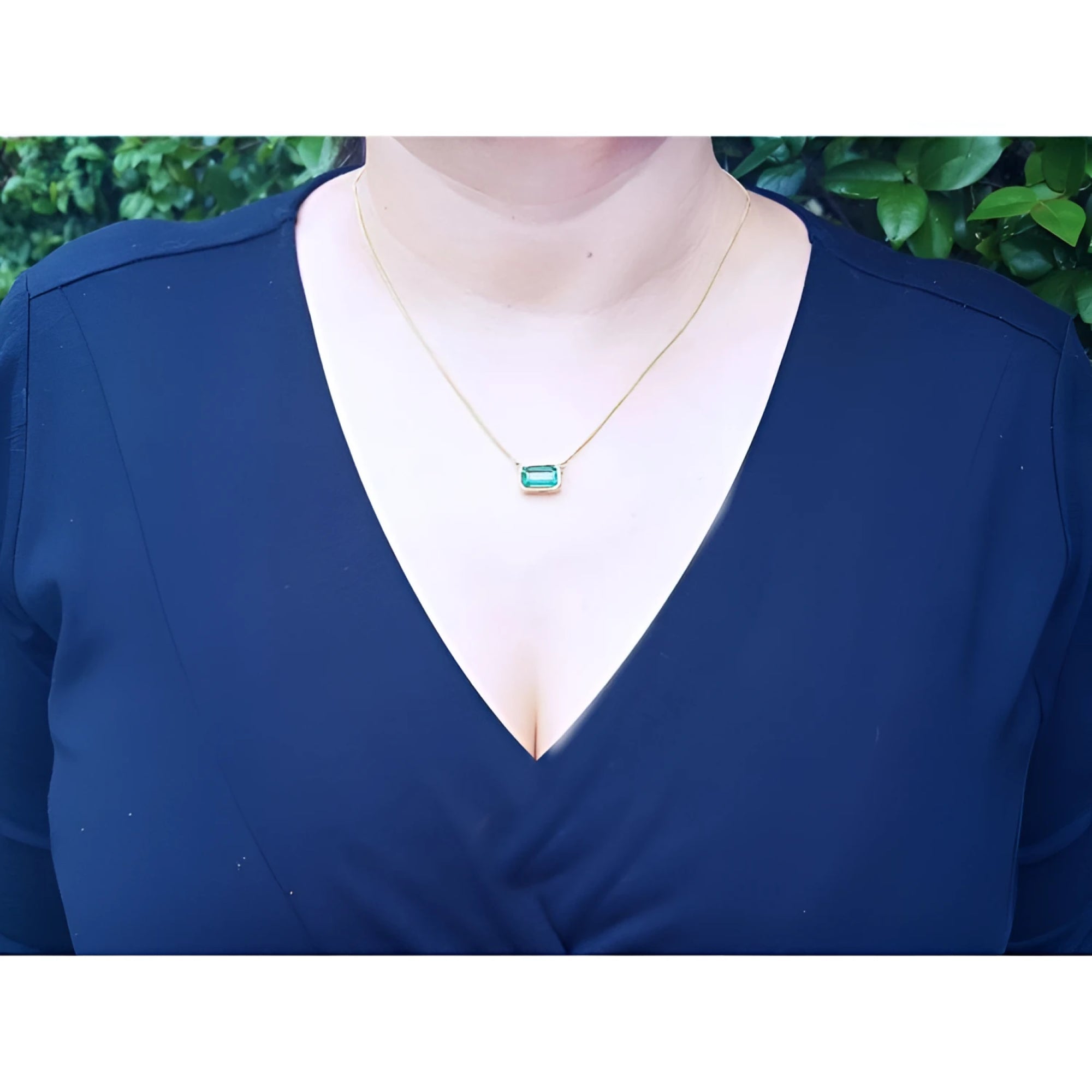 Woman wearing an 18K yellow gold necklace with a bezel-set, east-west emerald-cut bluish-green emerald.