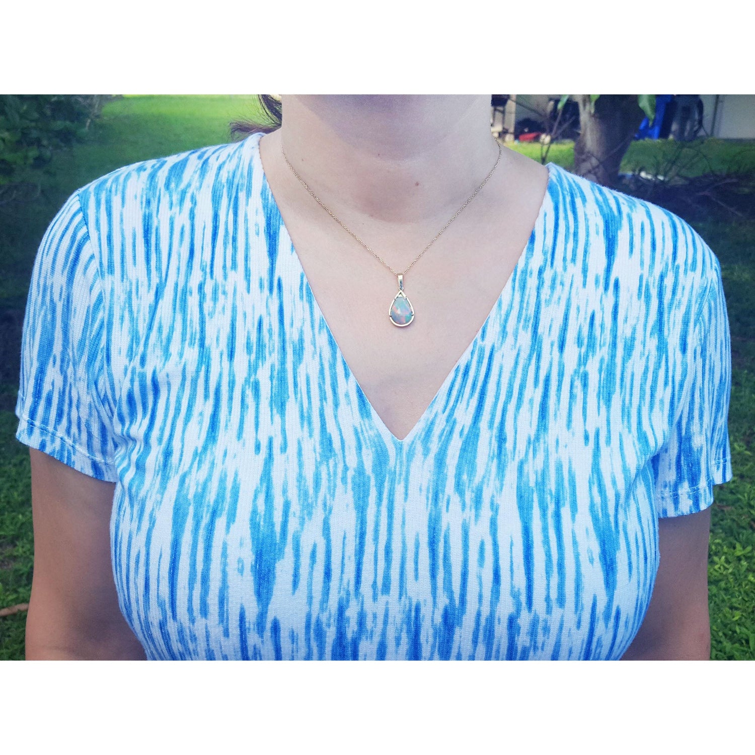Person wearing a blue and white patterned shirt with an Ethiopian opal pendant necklace outdoors.