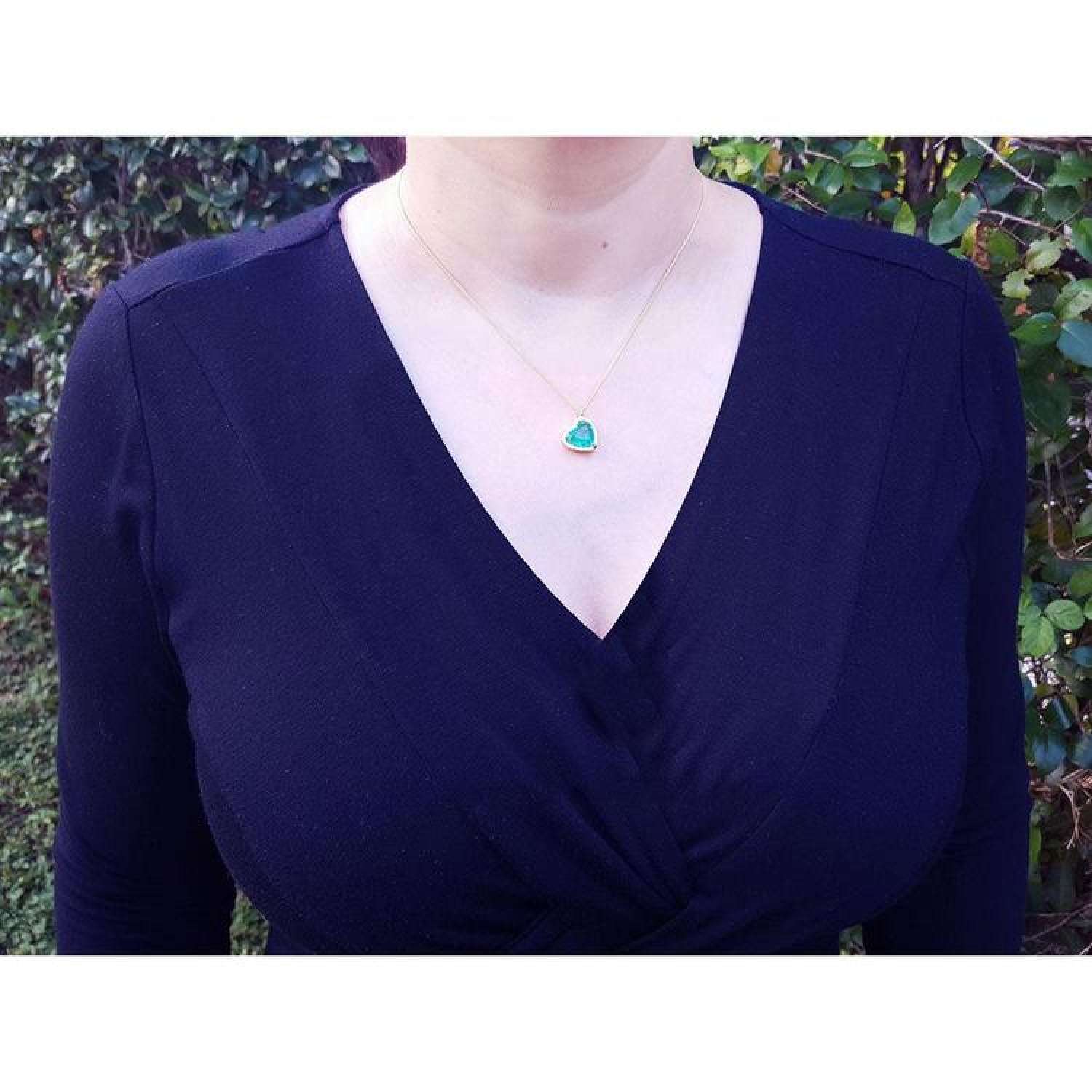 Tilted heart emerald necklace with halo diamonds in 18K yellow gold, worn on a model.