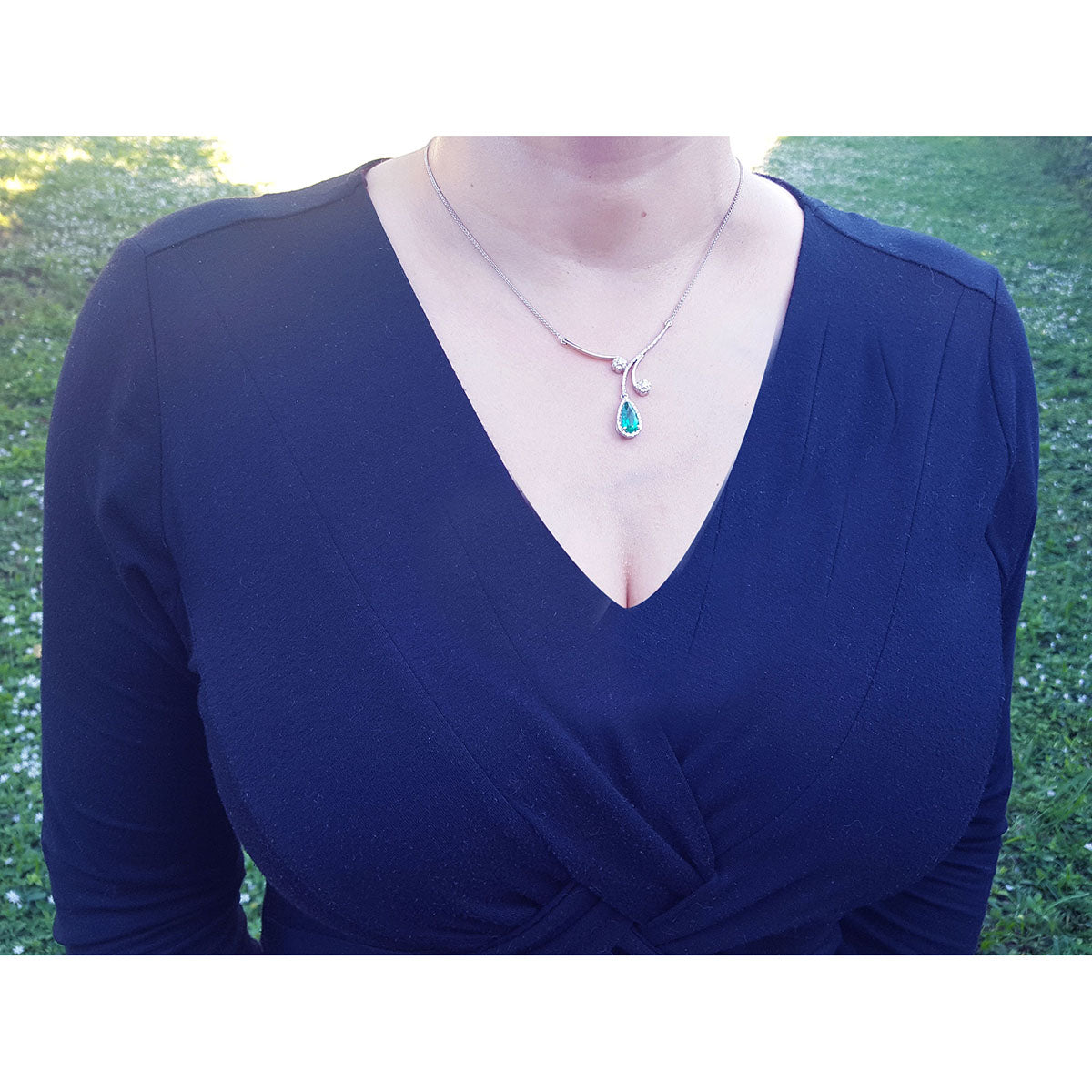 Woman wearing a blue dress with a white gold necklace featuring a natural emerald pendant against a grassy background