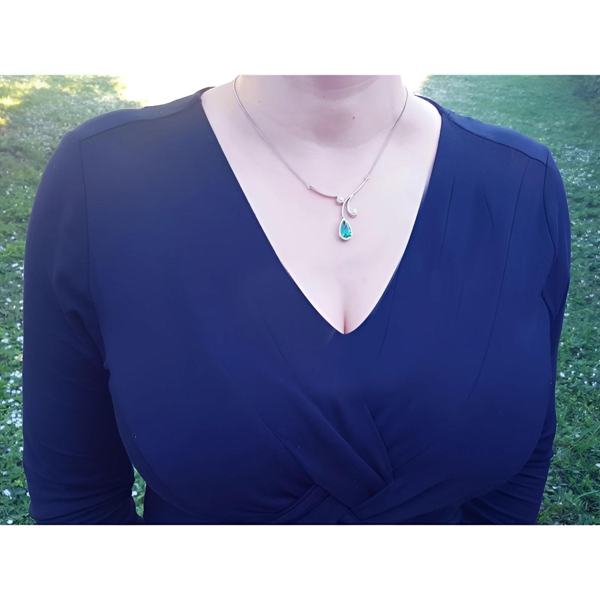 Pear cut natural emerald necklace with diamond halo in 18K white gold, worn on a dark blue dress.