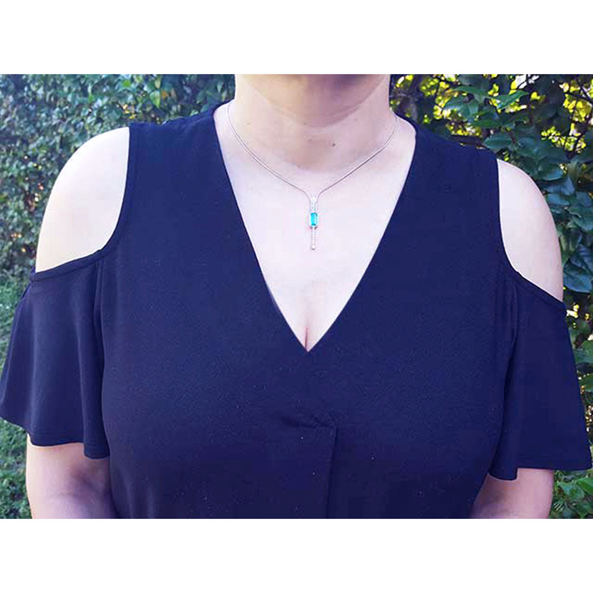 Woman wearing a navy blue dress with a Colombian emerald necklace against a green outdoor background