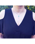 Woman wearing a navy blue dress with a Colombian emerald necklace against a green outdoor background