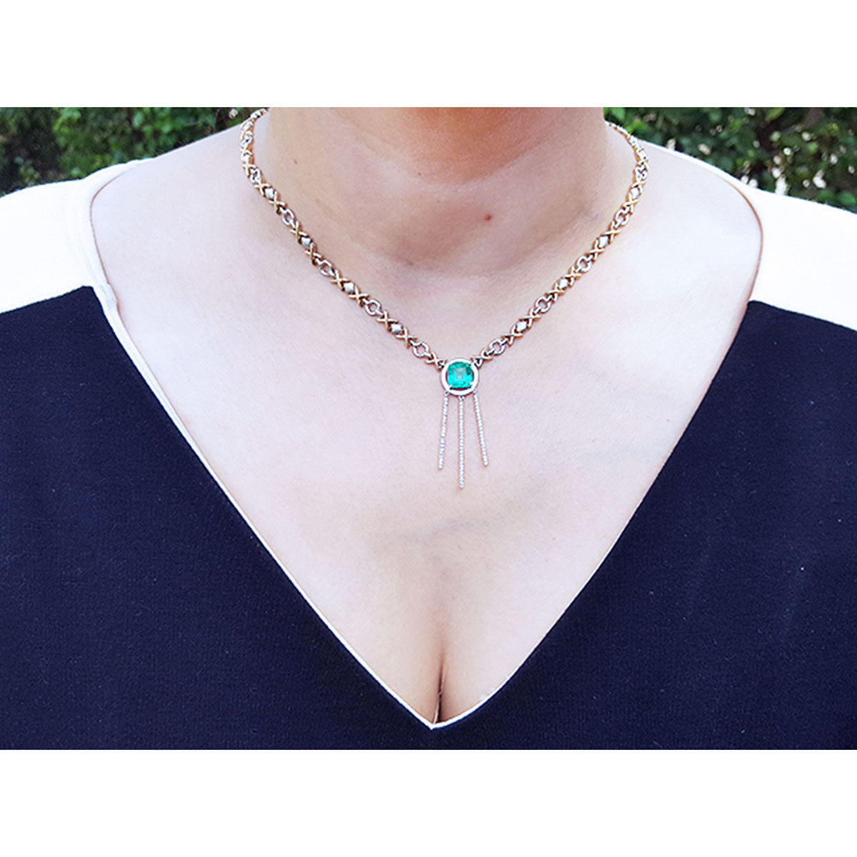 Kisses and hugs emerald necklace, square cut gemstone on a woman wearing a dark blue top.