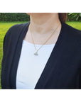 Person wearing a black cardigan over a white shirt with a necklace featuring an opal pendant outdoors.