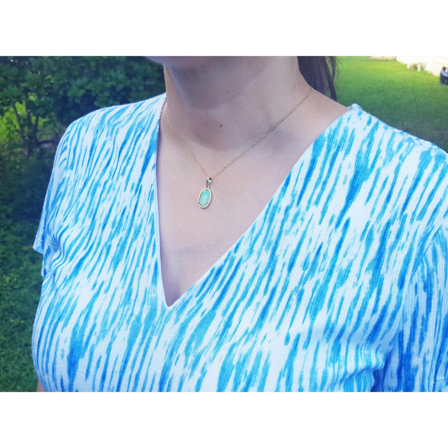 
A woman wearing a blue and white patterned top with a Ethiopian Welo opal gold necklace outdoors.