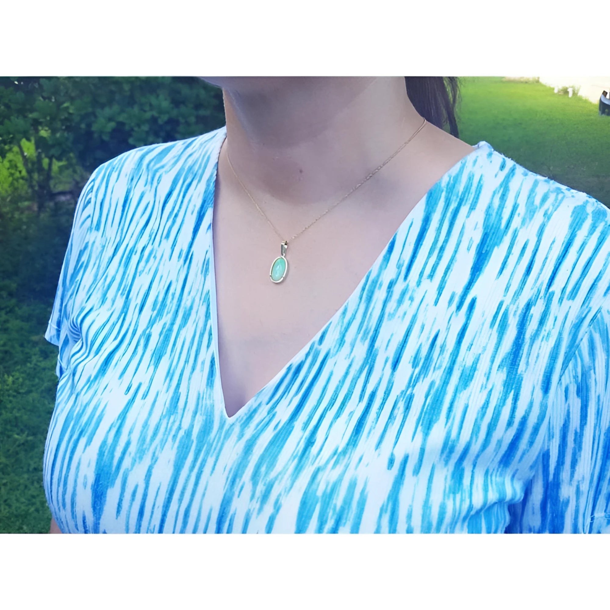 Ethiopian opal pendant with bluish-green hues, set in 14K yellow gold, worn on a woman's neck.