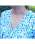 
A woman wearing a blue and white patterned top with a Ethiopian Welo opal gold necklace outdoors.