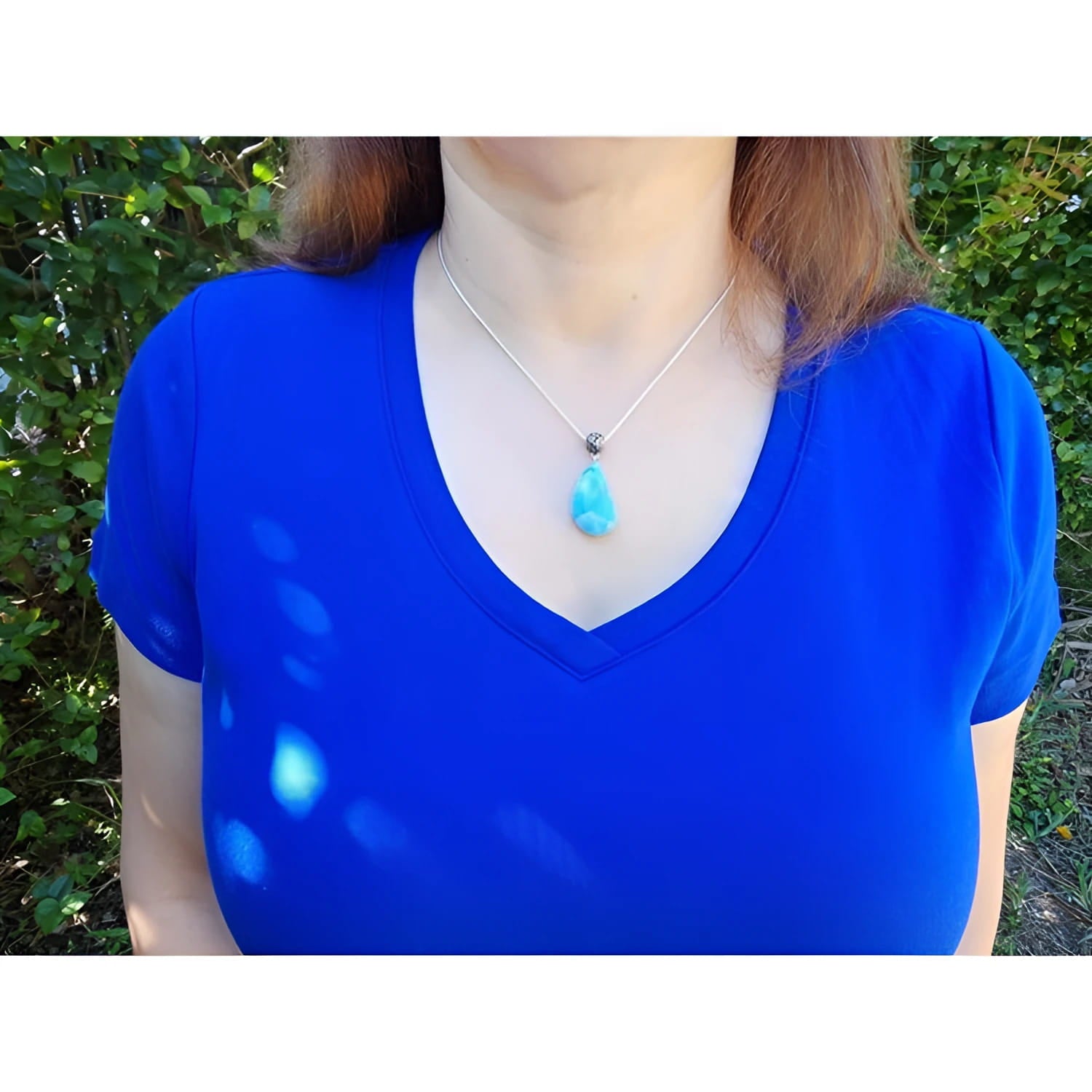 Vivid blue and white larimar teardrop pendant on a sterling silver necklace worn on a blue shirt.