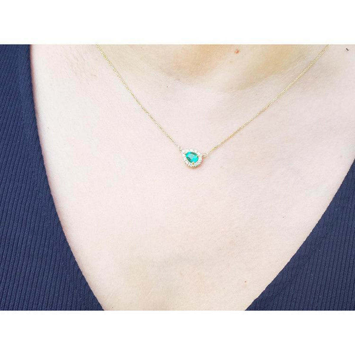 Vibrant pear-shaped emerald necklace with diamond halo on a delicate 14K yellow gold chain.