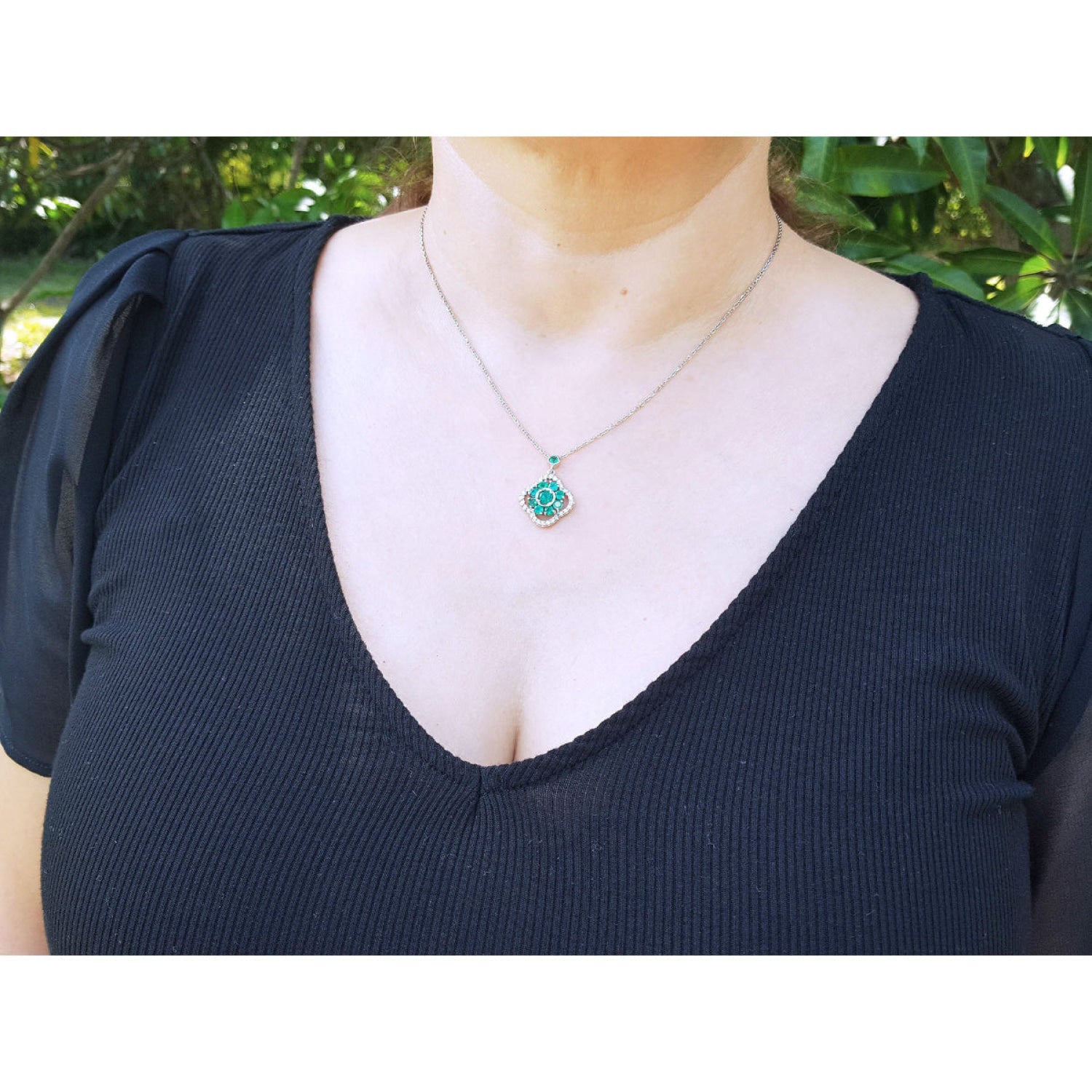 A close-up of a person wearing a 
14K white gold cluster necklace with natural Colombian emeralds and diamonds in a 4-leaf clover design.