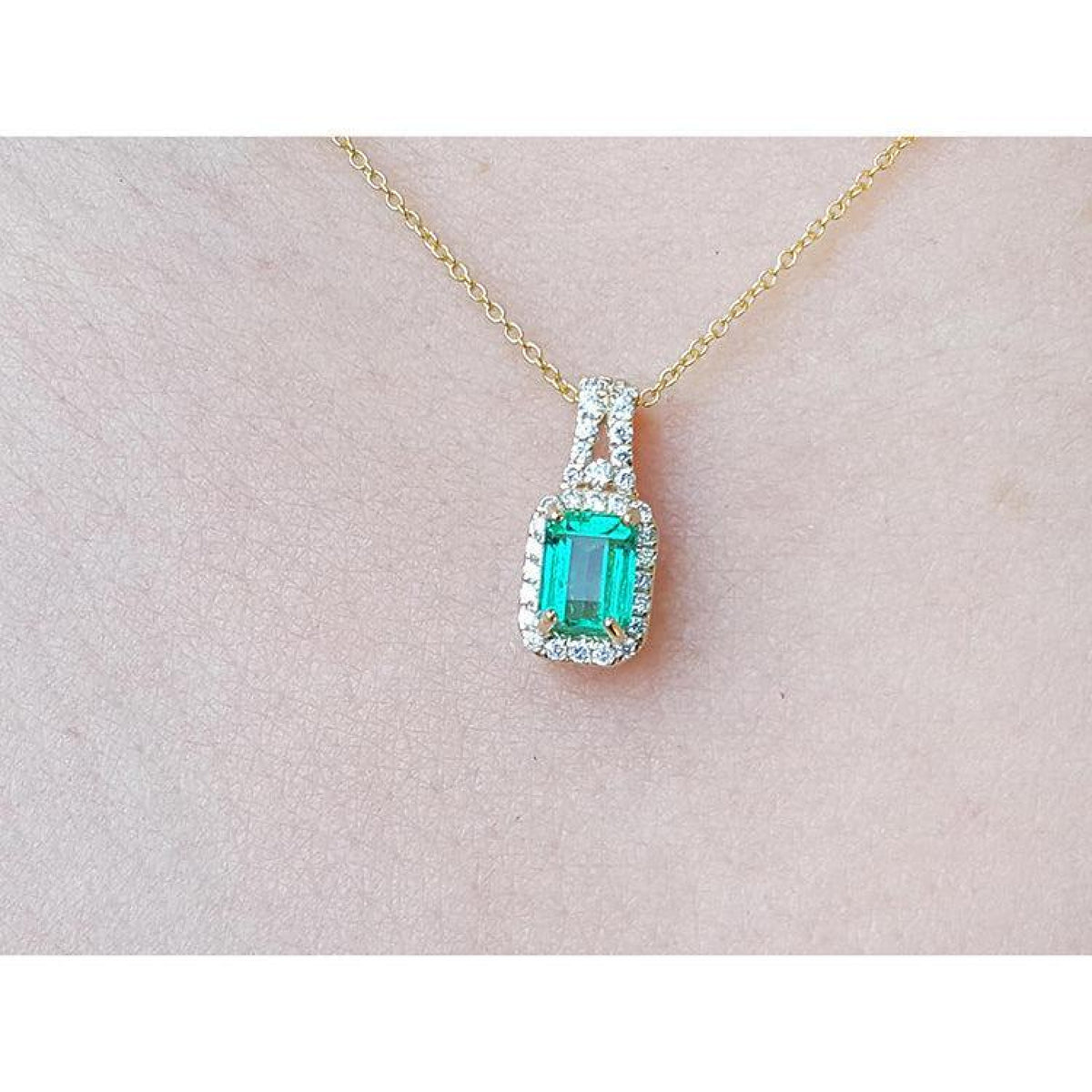 Emerald cut Colombian emerald pendant with halo diamonds on a 14K gold chain, worn on a neck.