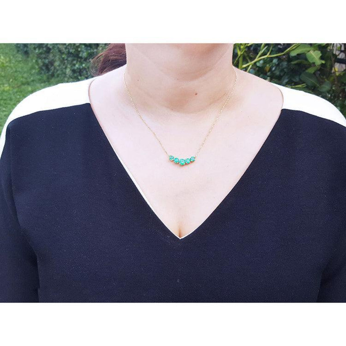 Woman wearing a 14K gold necklace with five round medium green Colombian emeralds.