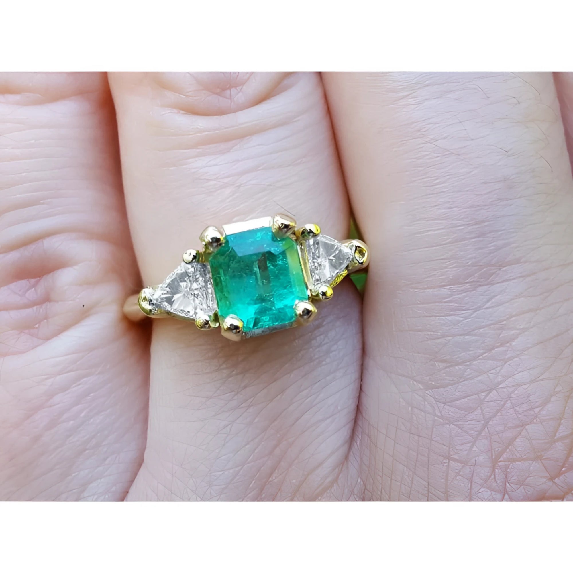 Square emerald and trillion side diamonds trillion cut ring made of 18k yellow gold on a finger.