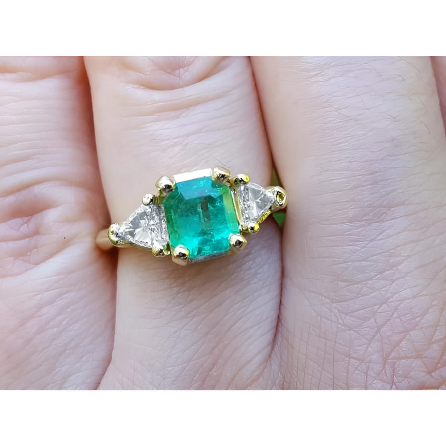 Square emerald and trillion side diamonds trillion cut ring made of 18k yellow gold on a finger.