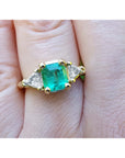 Square emerald and trillion side diamonds trillion cut ring made of 18k yellow gold on a finger.