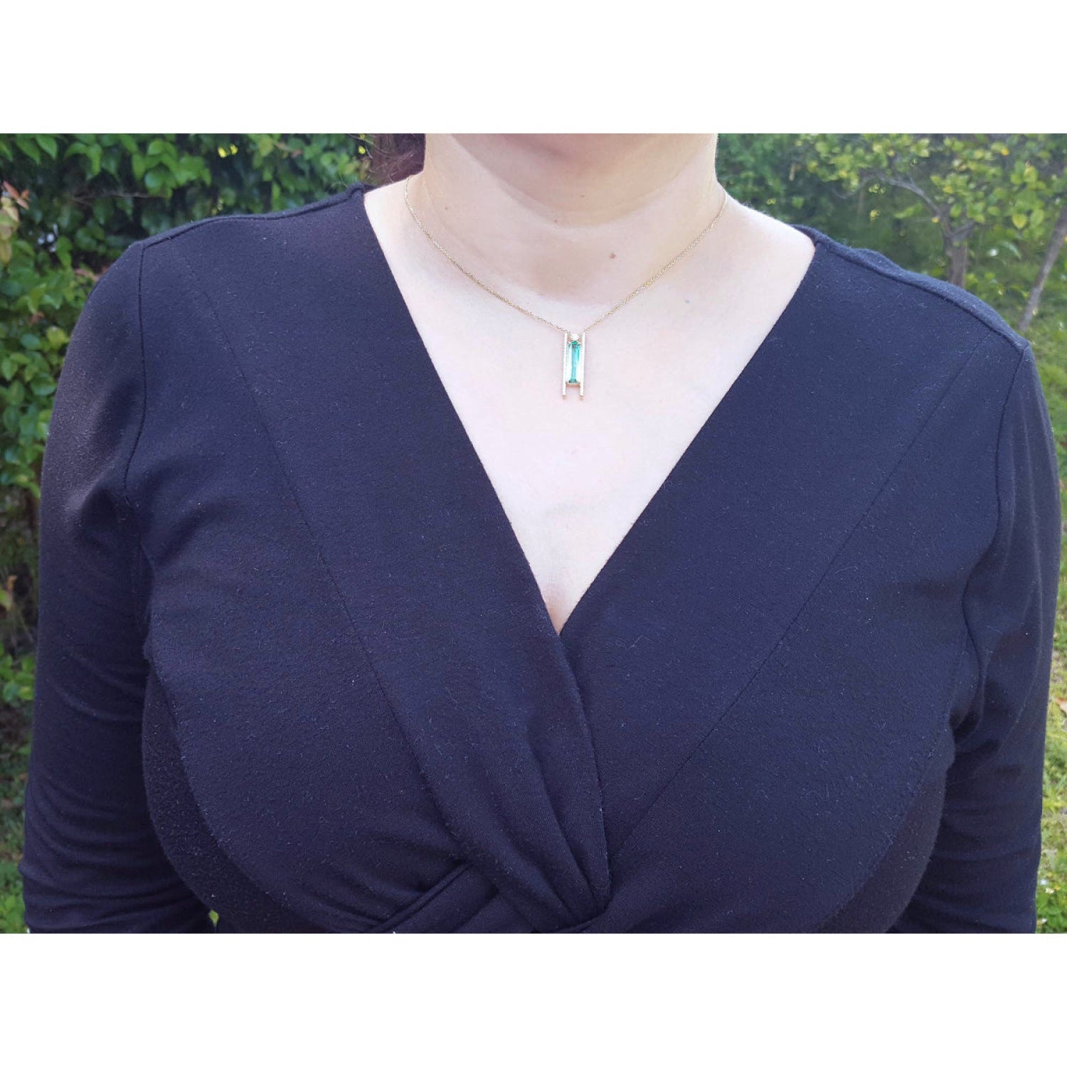 Emerald baguette cut necklace with natural diamonds, 14K yellow gold, worn on a black top.