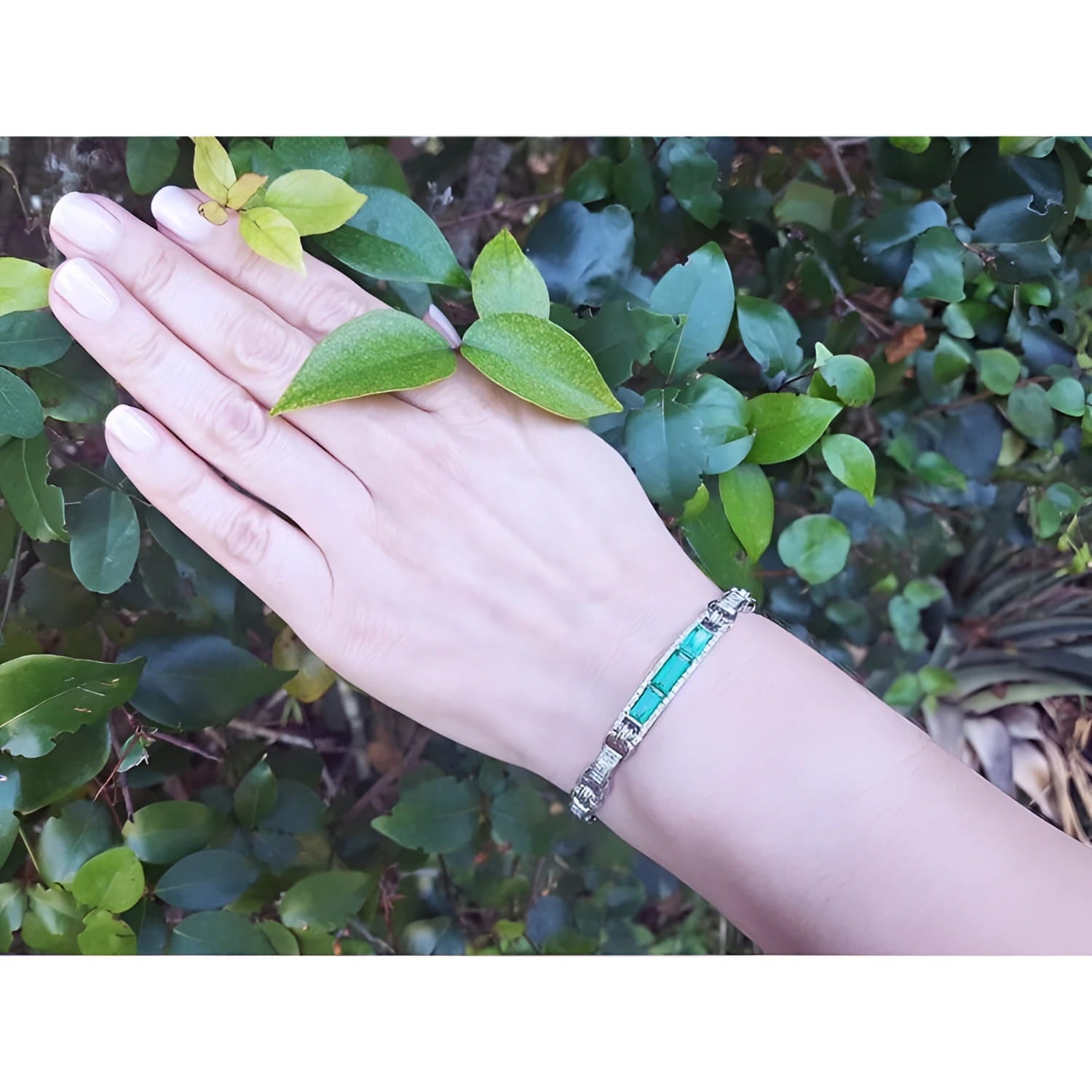 Hand wearing a bracelet with vibrant Colombian emeralds and princess cut diamonds.