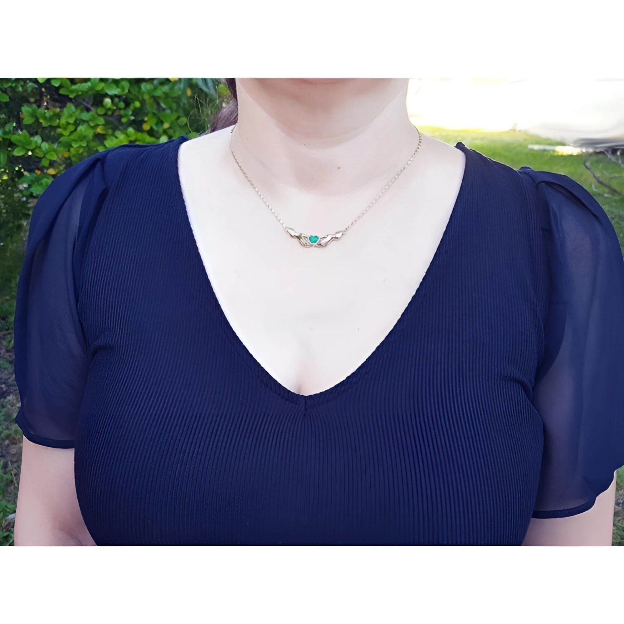 Woman wearing a blue top with puffed sleeves and a Claddagh emerald heart necklace outdoors.